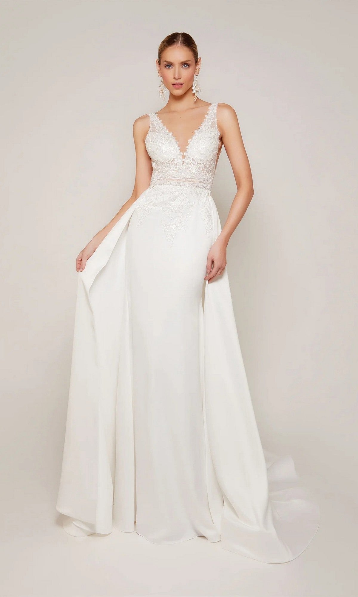 A woman wears the Alyce 7097 long formal dress featuring a sleeveless lace appliqué bodice, deep V-neckline, and flowing skirt against a plain background.